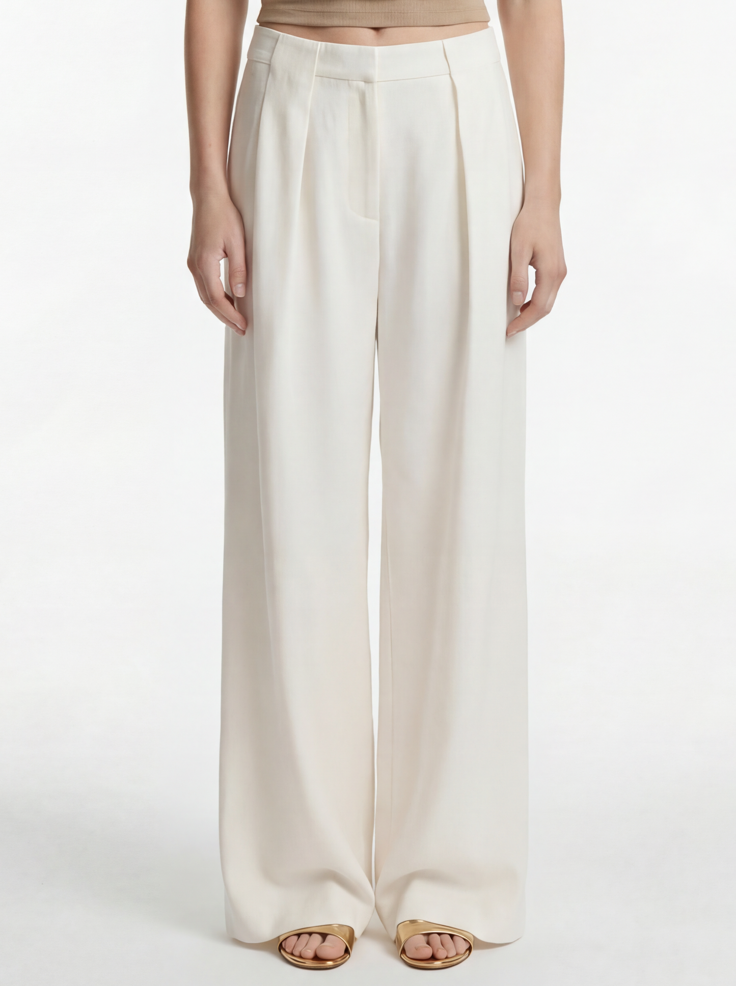 Woman wearing a beige sleeveless top and white pants on a white background