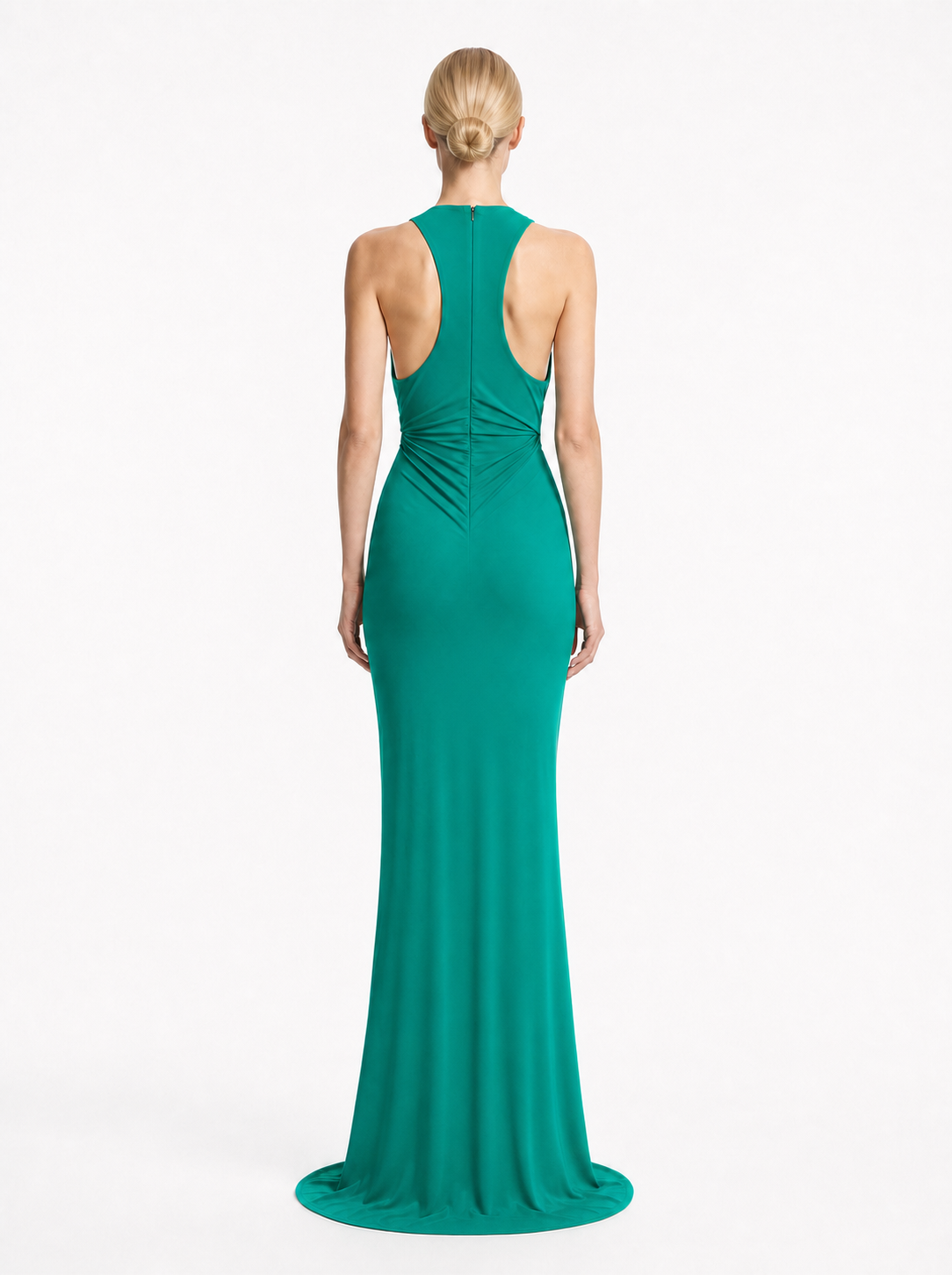 A woman modeling a floor-length teal green gown from the back, showing a high open back, ruched waist, and slight train on a plain light gray studio background.