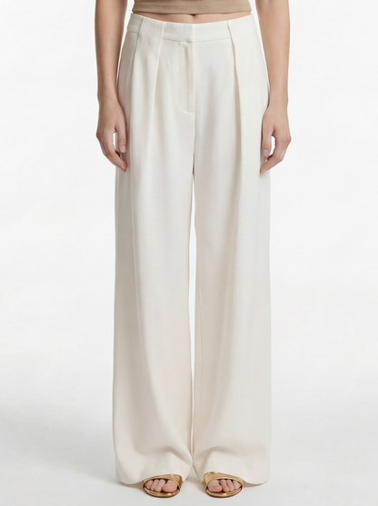 Woman wearing a beige sleeveless top and white pants on a white background
