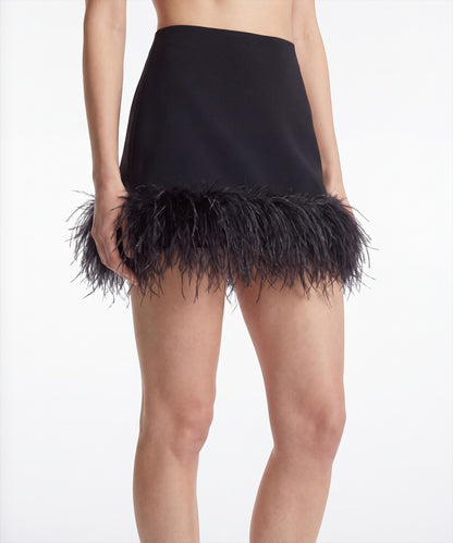 Merdulie black mini skirt with a fitted silhouette and dramatic feather trim hem on a model against a white background